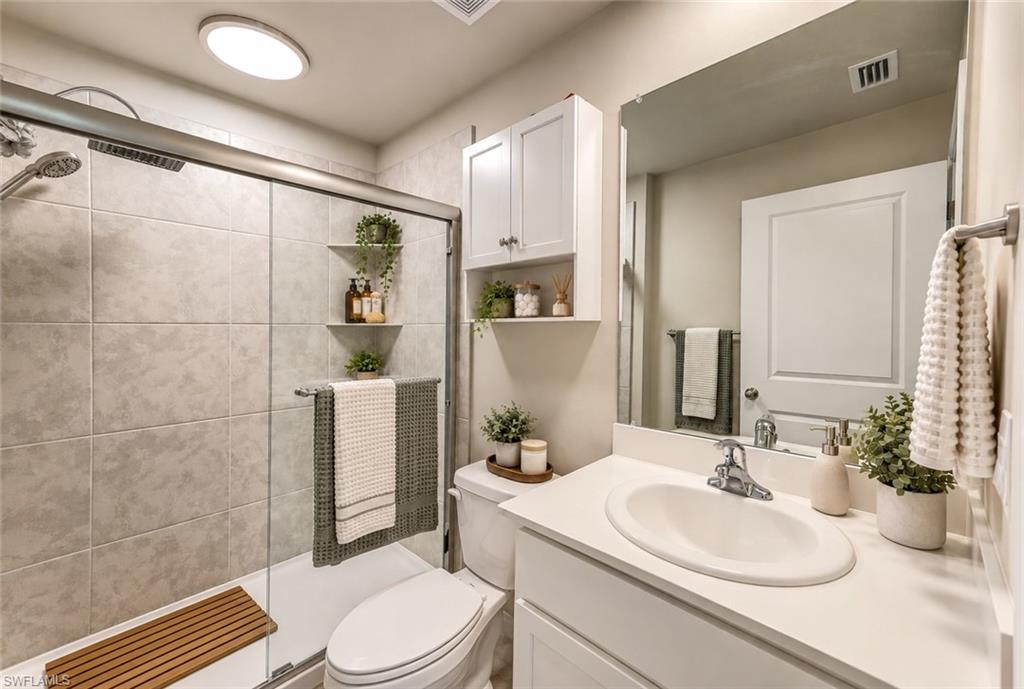Bathroom with a glass shower, tiled walls, built-in shelves, and a white vanity.