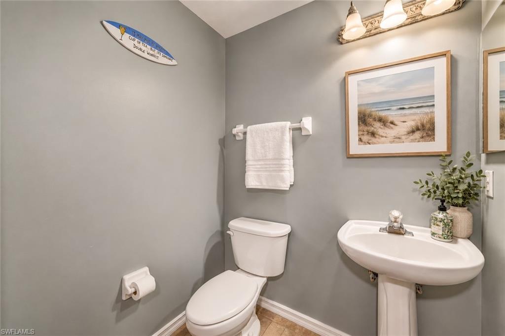 Gray bathroom with a white toilet, pedestal sink, and framed beach artwork.