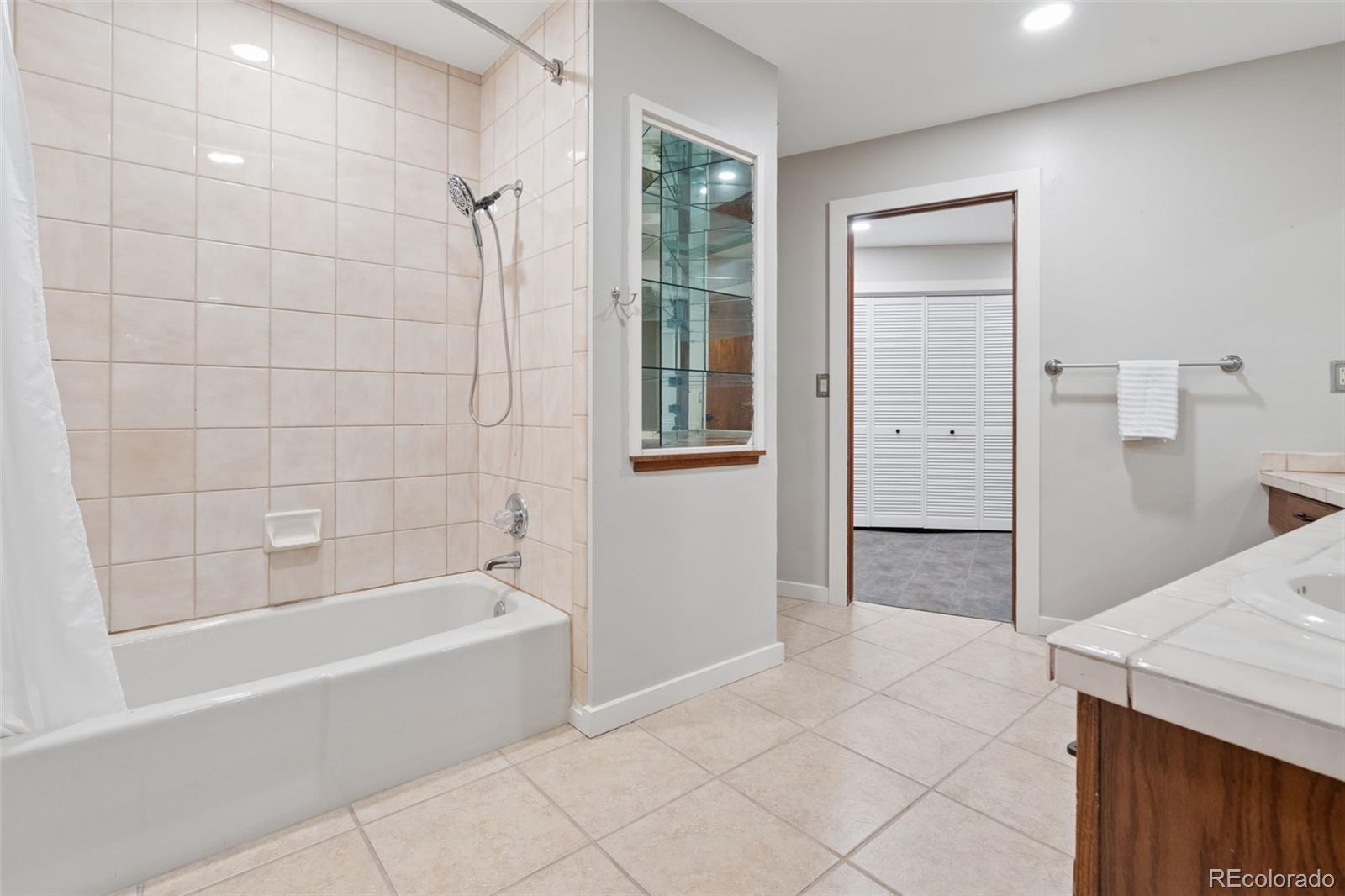 Bathroom with tiled tub and shower, vanity, and doorway to a closet with louvered doors.