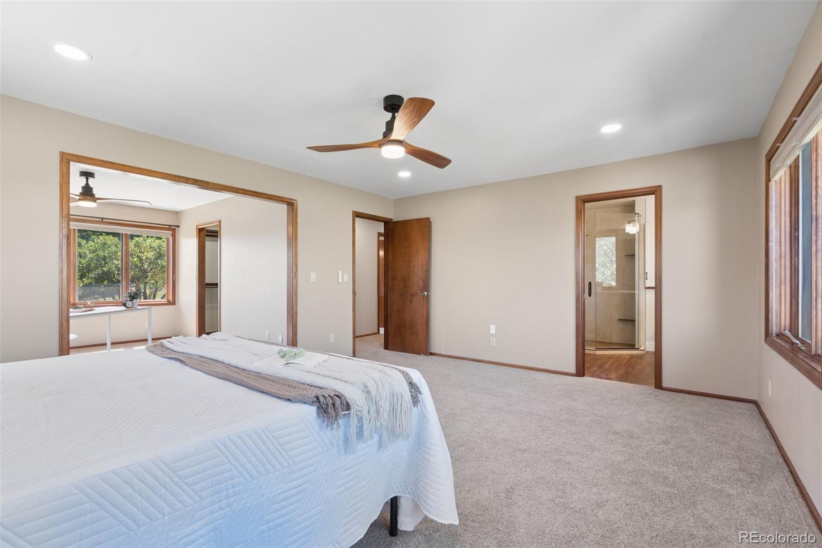 Spacious bedroom with a white bed, wood-blade ceiling fan, and doorway to a glass-enclosed shower.