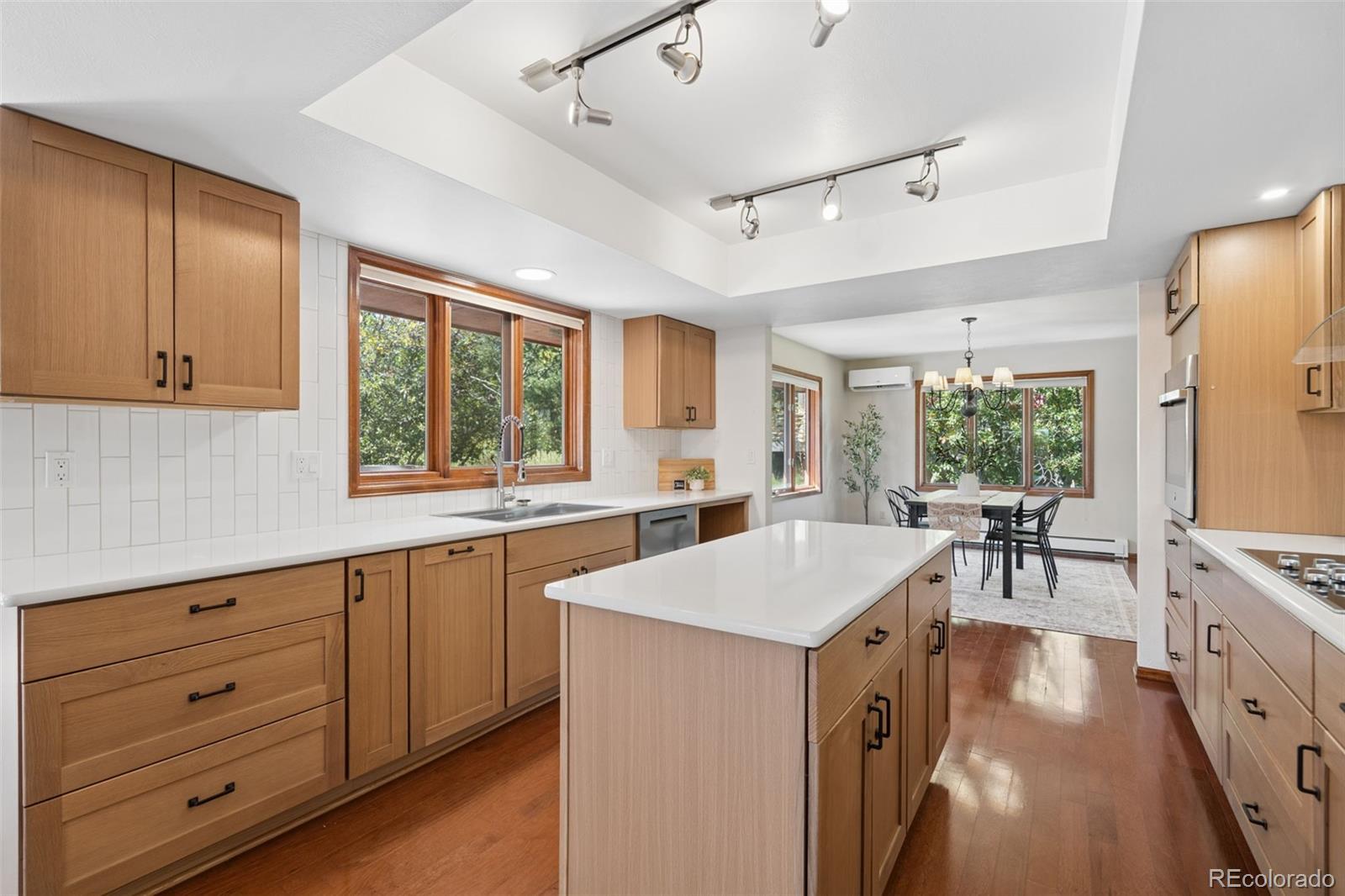 Kitchen with warm wood cabinetry, a large island, and dining area by leafy windows.