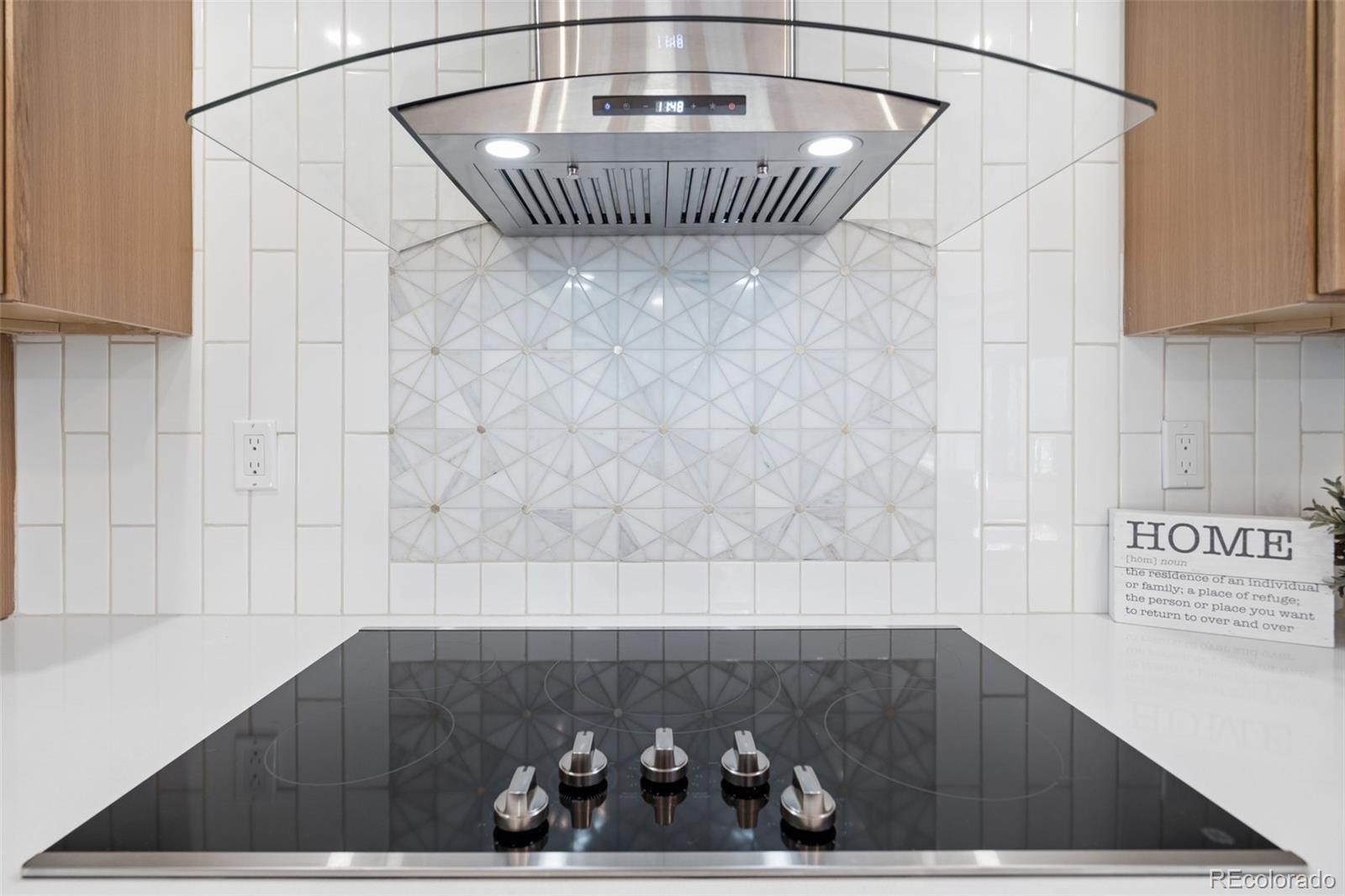 Kitchen cooktop and stainless range hood against a geometric white tile backsplash.