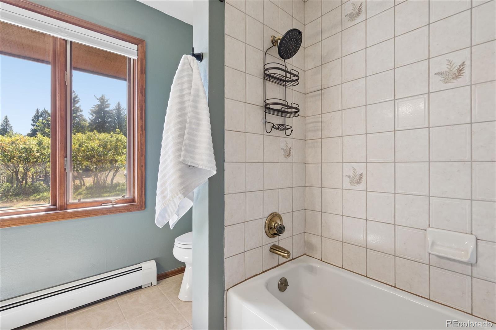 Bathroom with a tiled bathtub and shower, a wood-trimmed window, and a white towel.