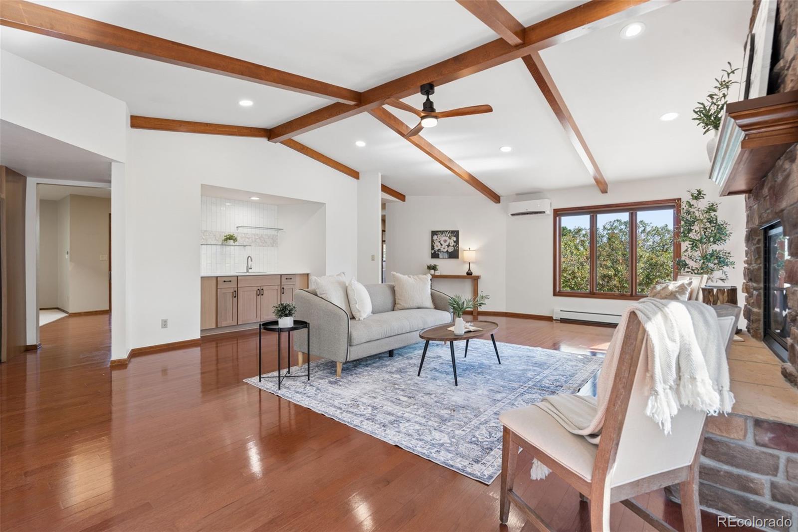 Living room with exposed wood ceiling beams, stone fireplace, and a sink-and-cabinet alcove.