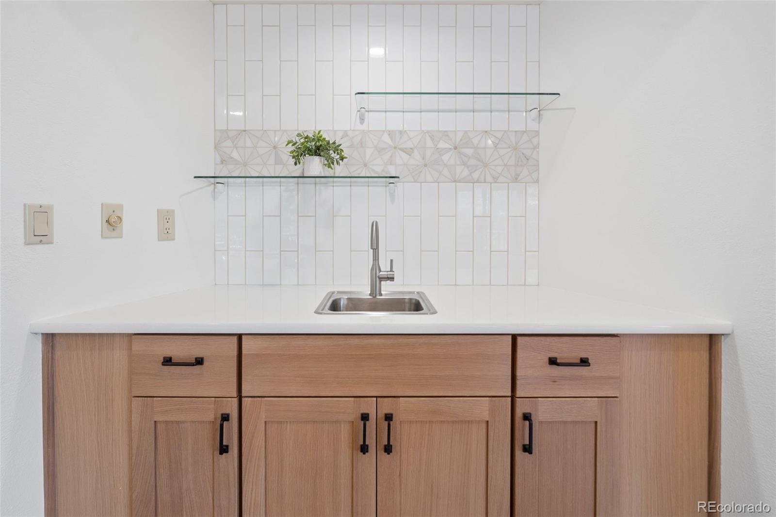 Kitchen sink with light wood cabinets, white countertop, and geometric tile backsplash.