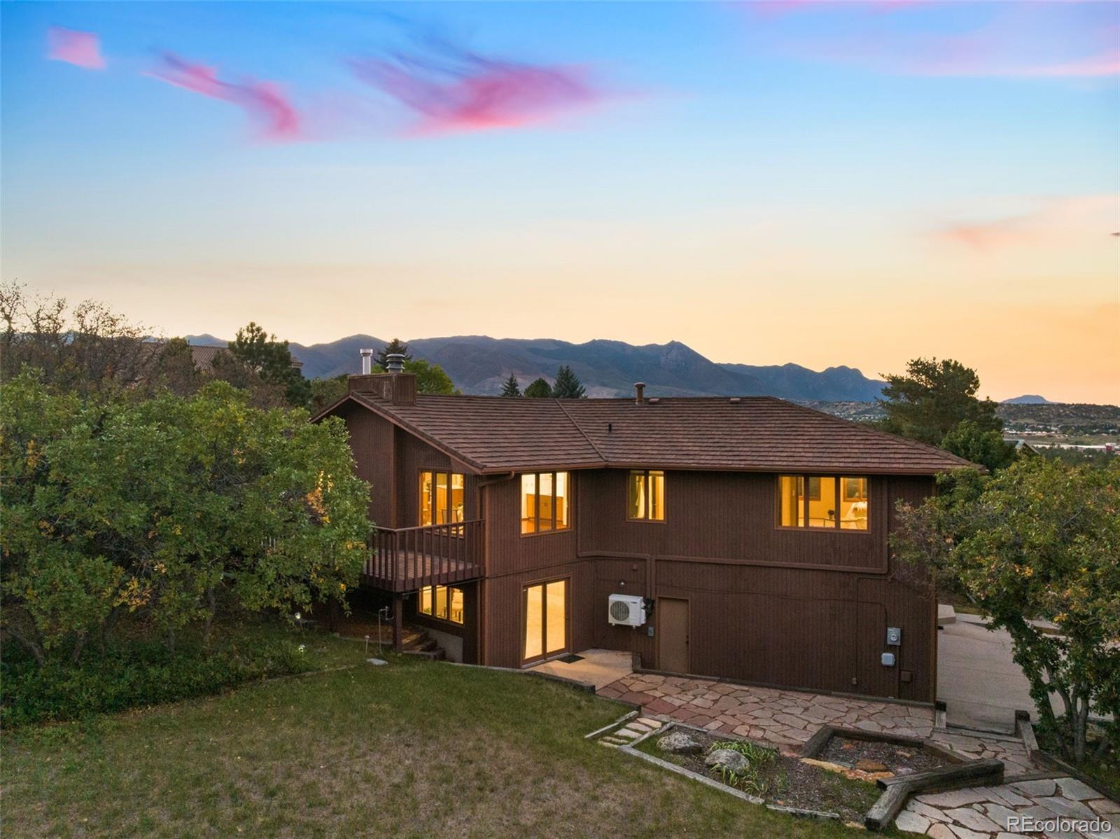 Brown two-story home with a stone patio and mountain views at dusk.
