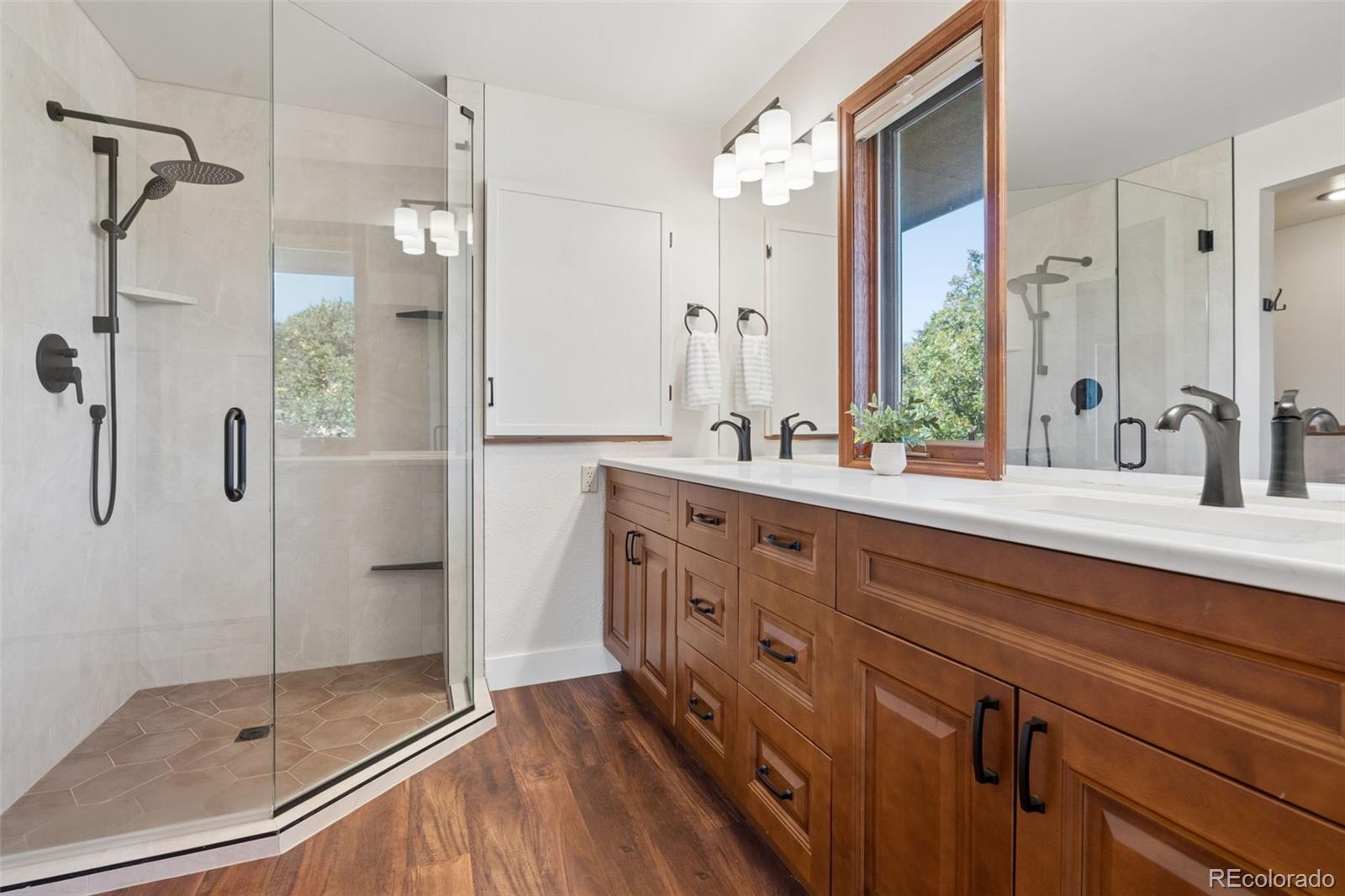 Bathroom with a glass walk-in shower and long wooden double vanity beneath a large window.