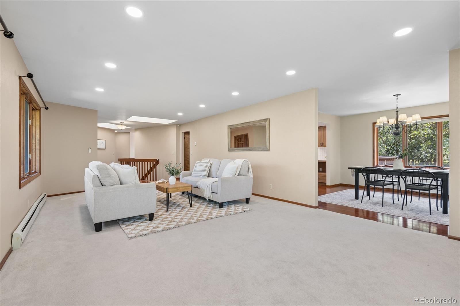 Open-plan living and dining area with white sofas, recessed lights, and large windows.