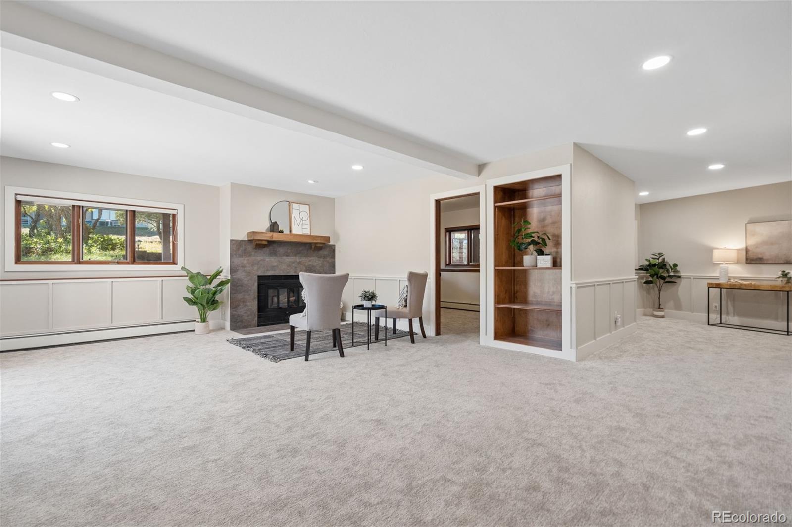 Carpeted living room with a stone fireplace, built-in shelves, and large windows.