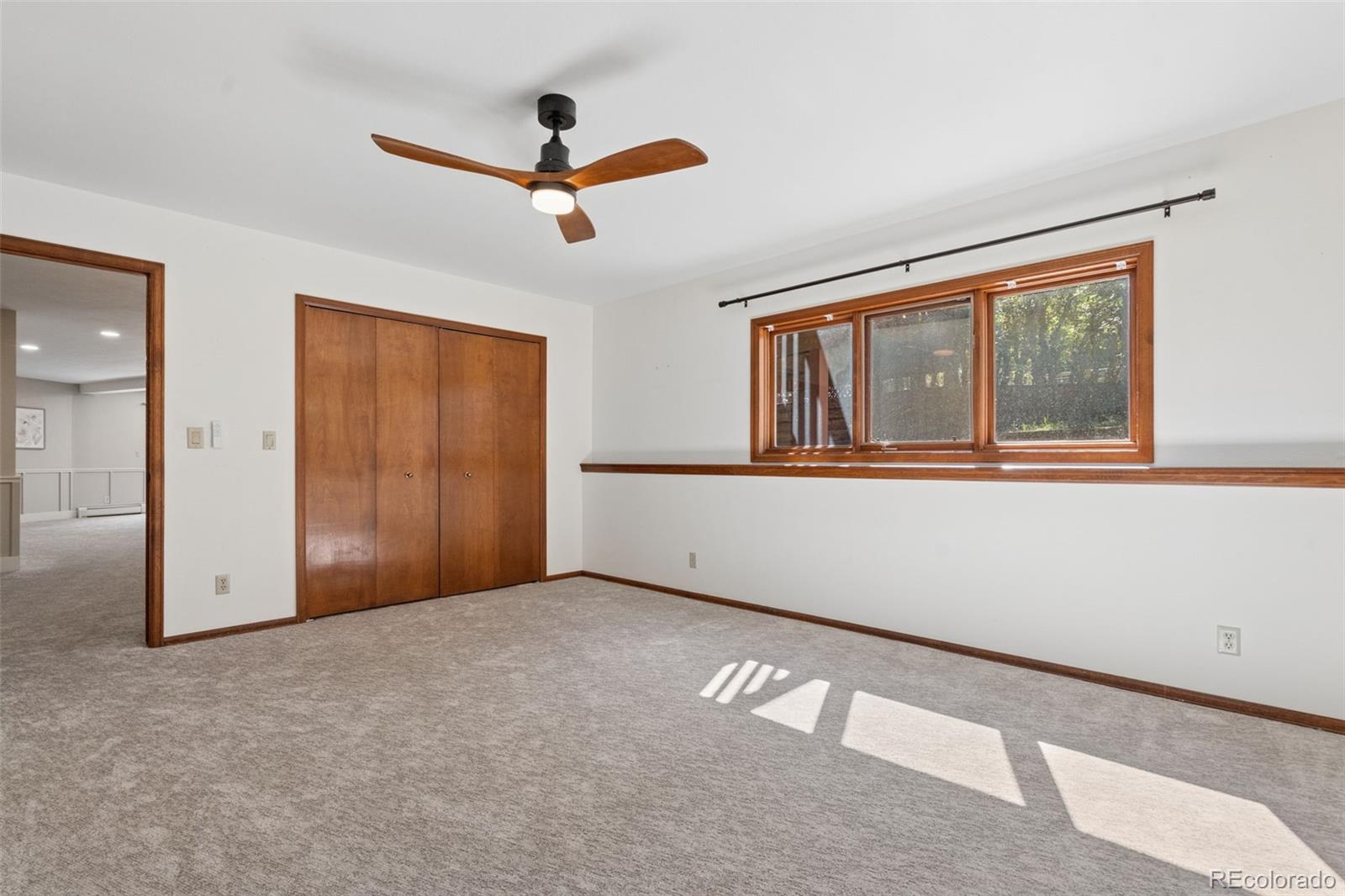 Vacant carpeted bedroom with a wood-trimmed window, double closet doors, and ceiling fan.