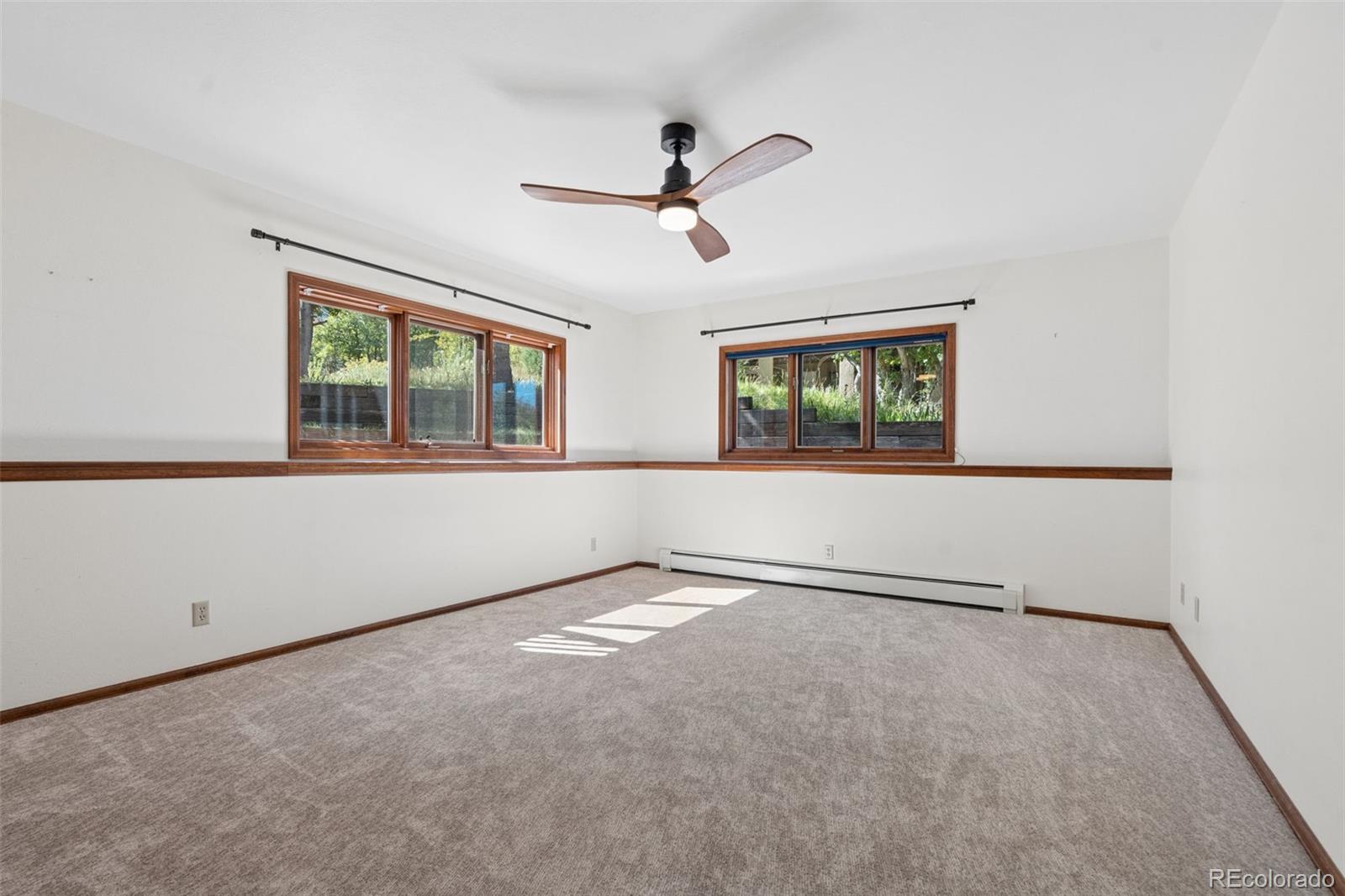 Empty carpeted room with two wood-framed windows and a ceiling fan.