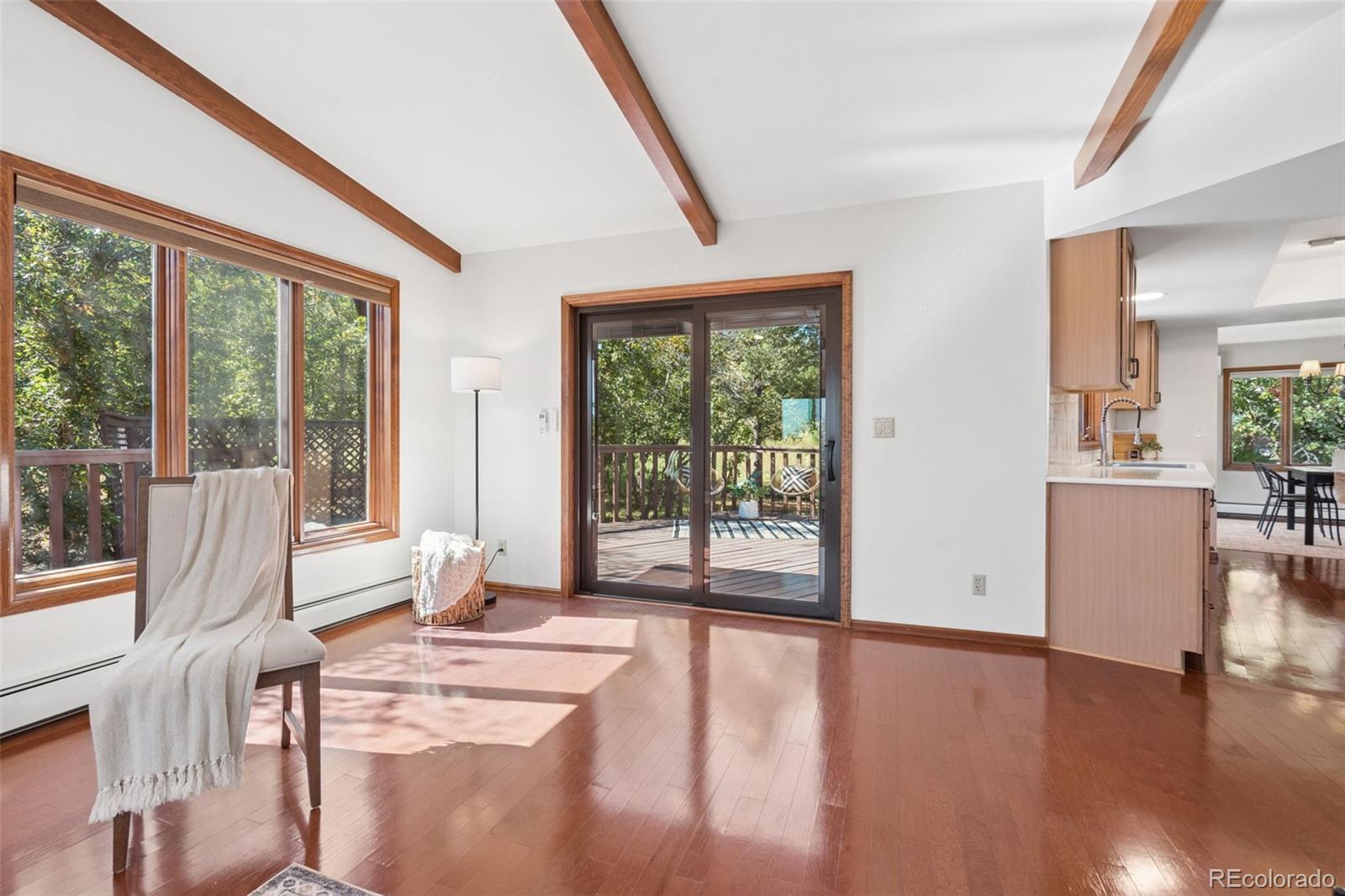 Living room with vaulted wood-beamed ceiling, hardwood floors, and sliding doors to a wooded deck.
