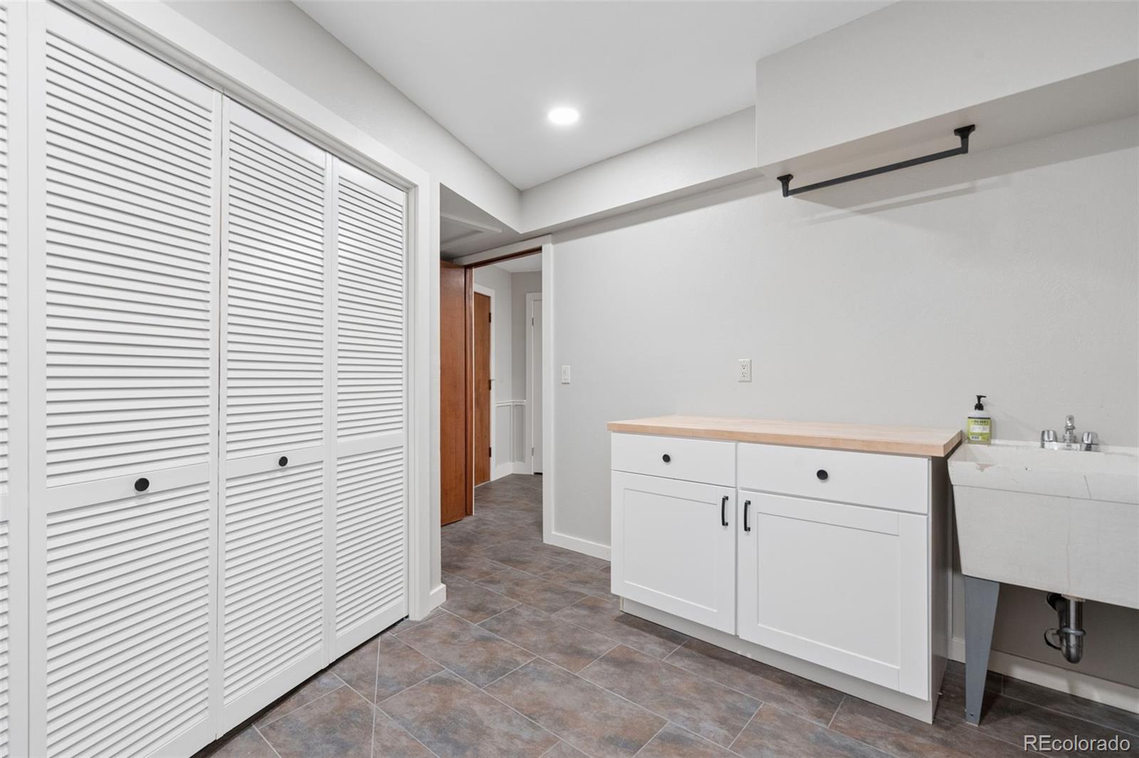 Laundry room with louvered closet doors, white cabinets, a wood countertop, and a utility sink.