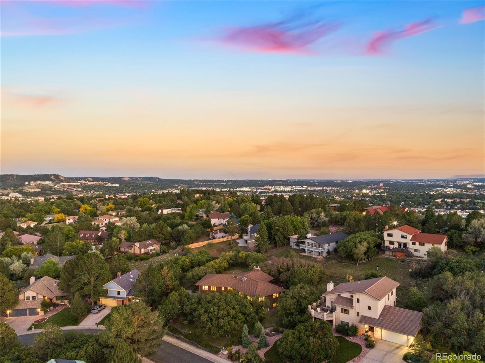 Aerial view of a leafy neighborhood and distant city beneath a colorful sunset sky.