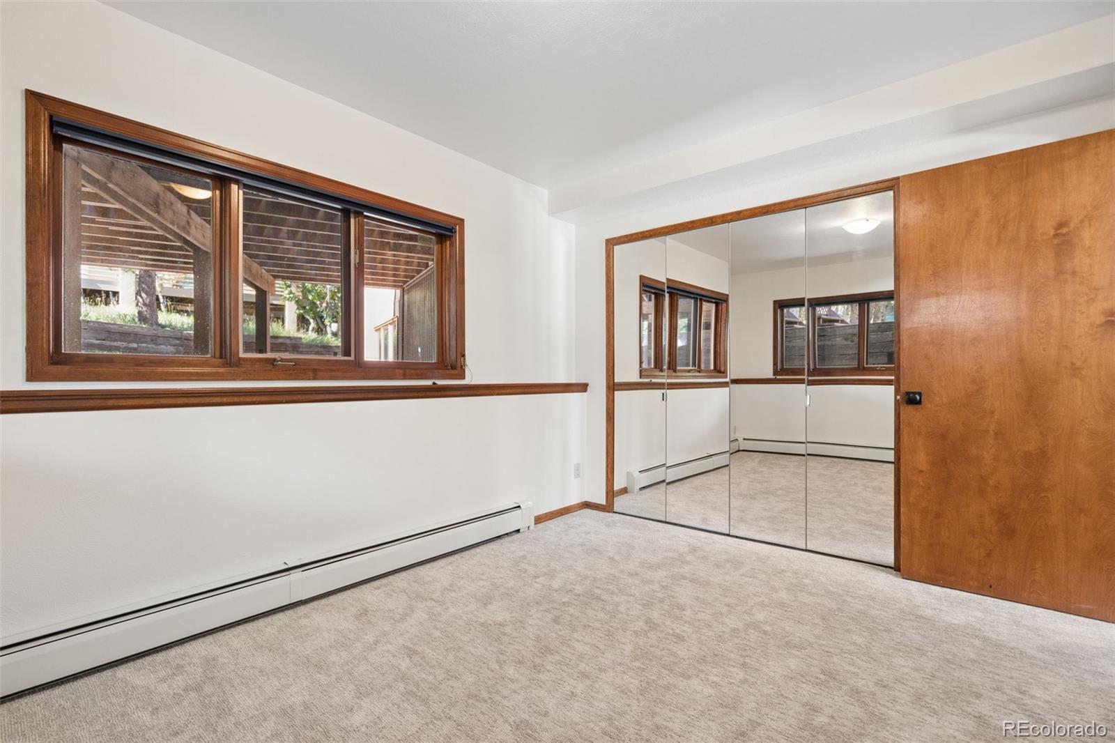 Empty bedroom with mirrored closet doors, a wide window, and light carpet.