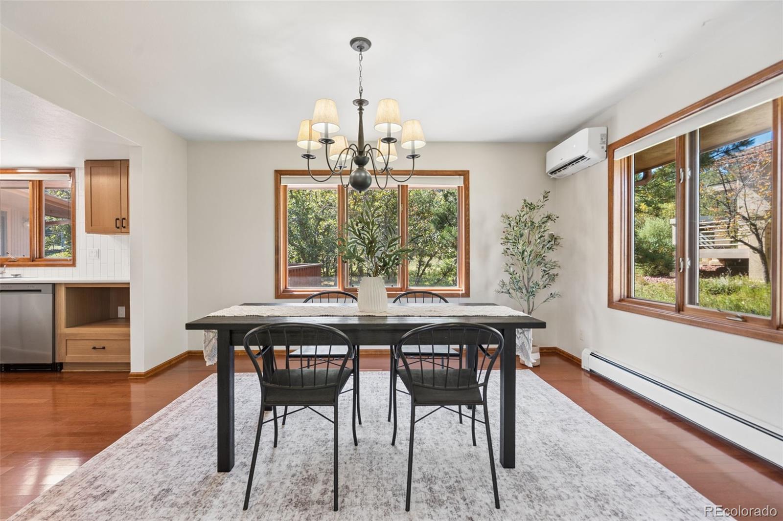 Dining room with a dark table, black chairs, and wood-trimmed windows overlooking leafy trees.