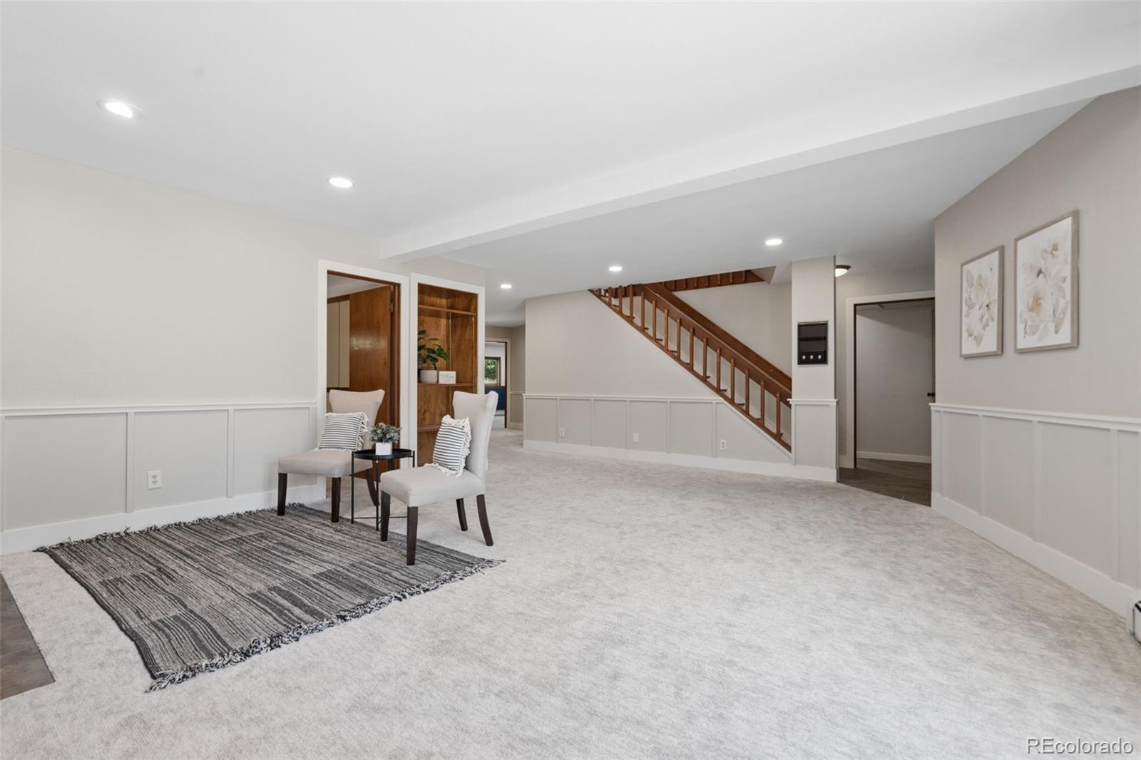 Staged basement living area with a wood staircase, built-in shelving, and two chairs on a striped rug.