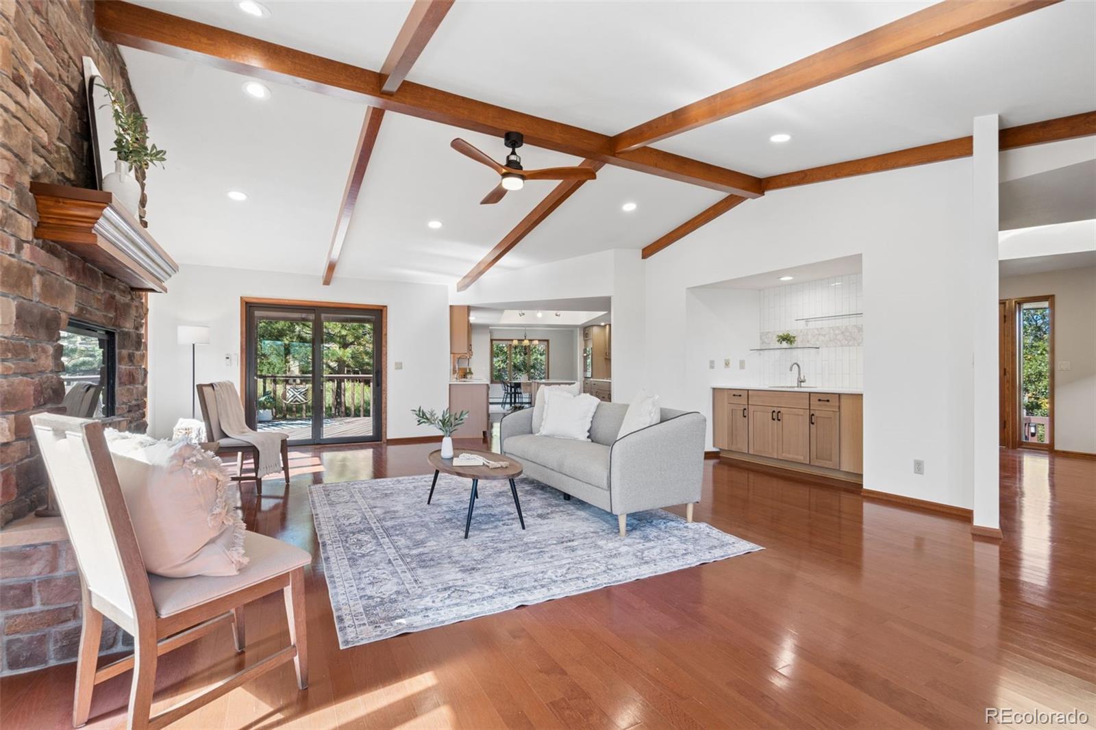 Living room with a stone fireplace, exposed wood ceiling beams, and hardwood floors.