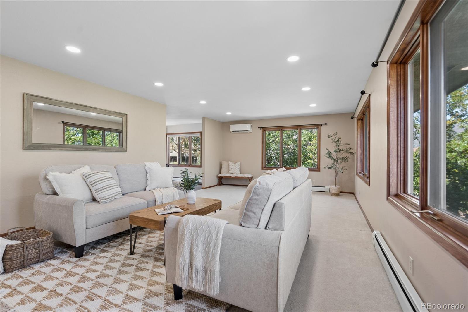 Staged living room with gray sofas, a patterned rug, and large wood-trimmed windows.