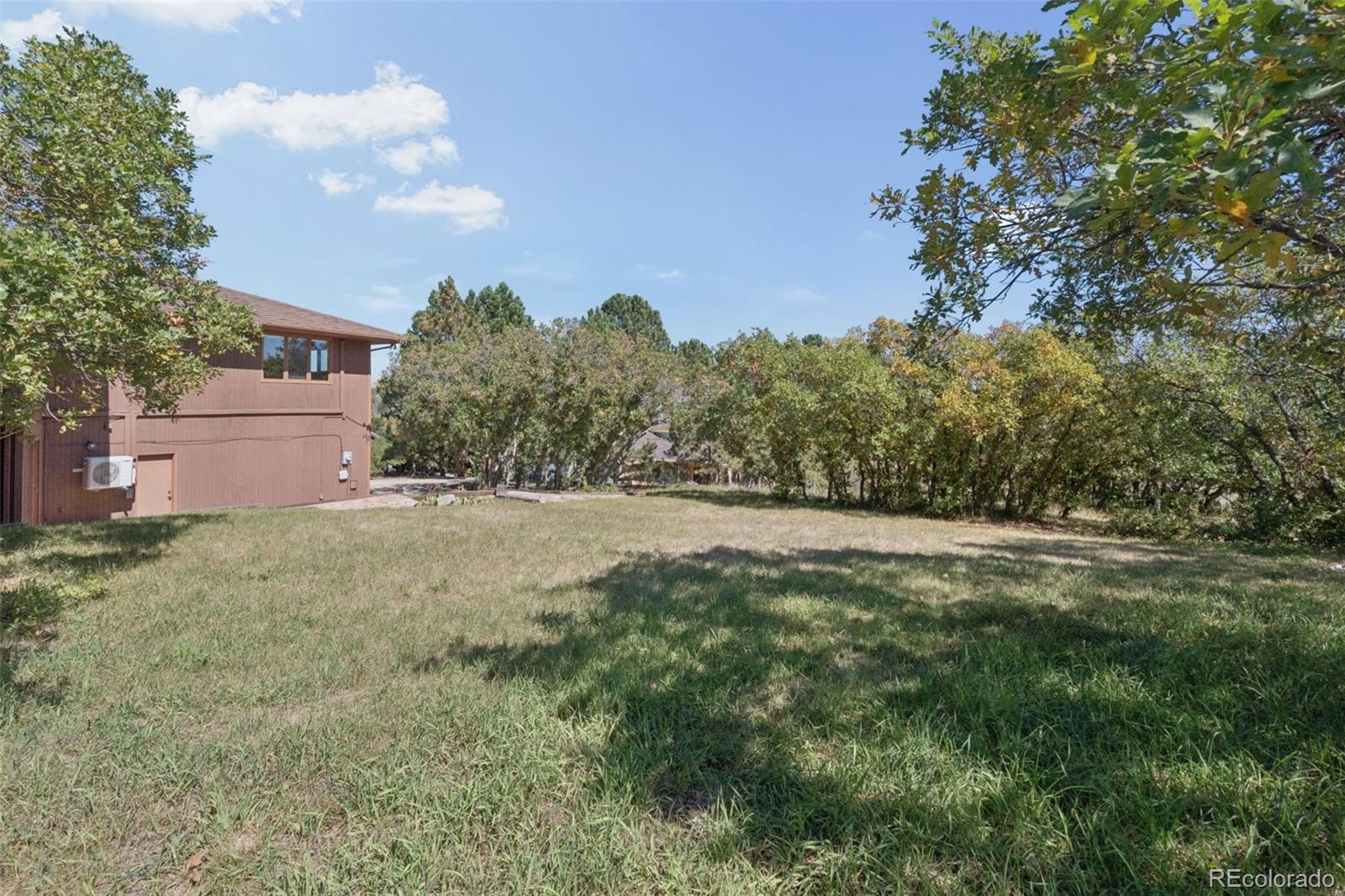 Brown two-story home beside a grassy yard bordered by mature trees.