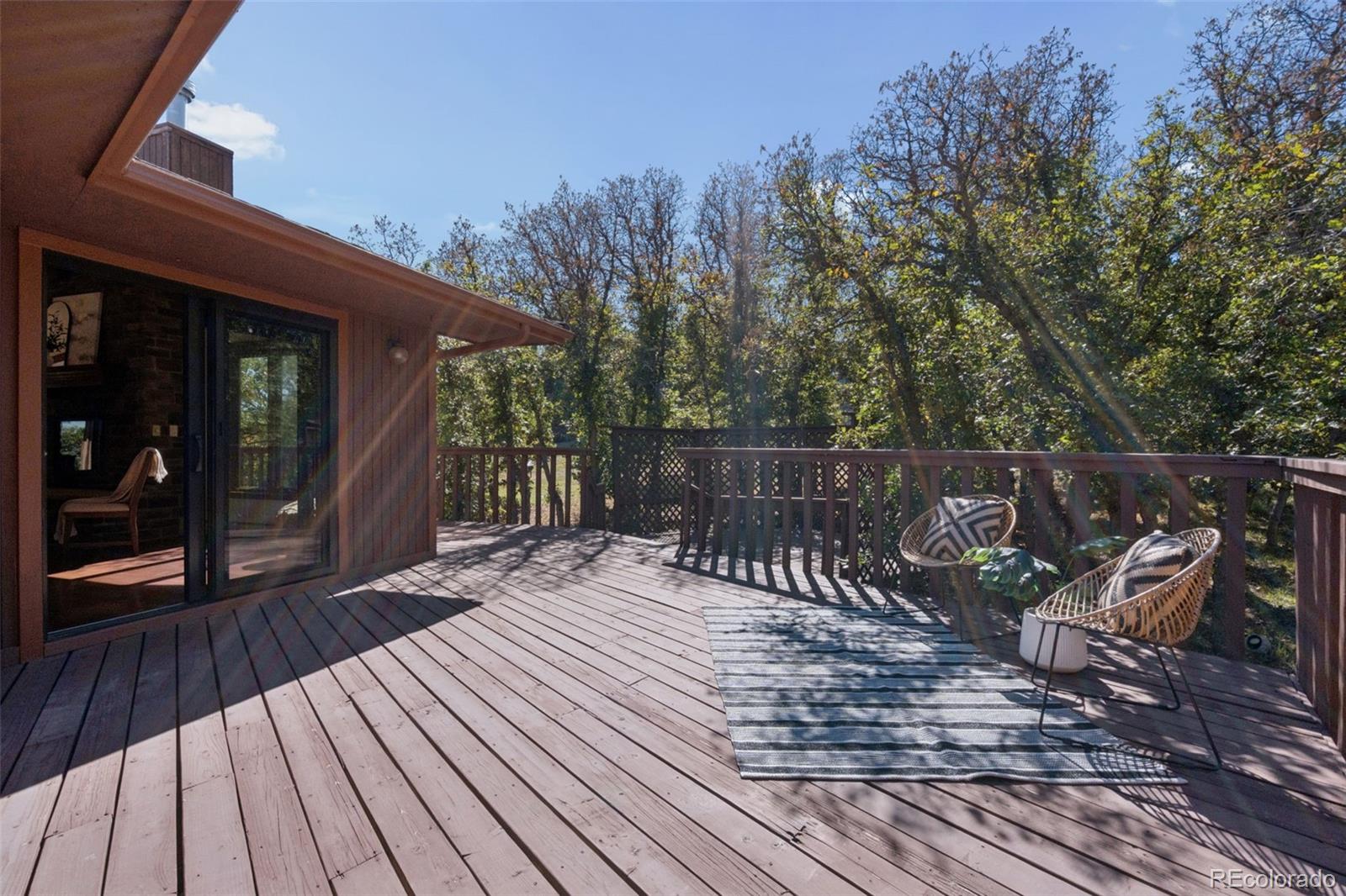 Wooden deck with woven chairs and a striped rug overlooking autumn woodland.