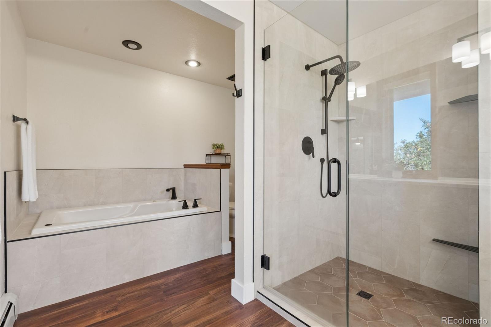 Bathroom with a built-in soaking tub beside a glass-enclosed shower with dark fixtures.