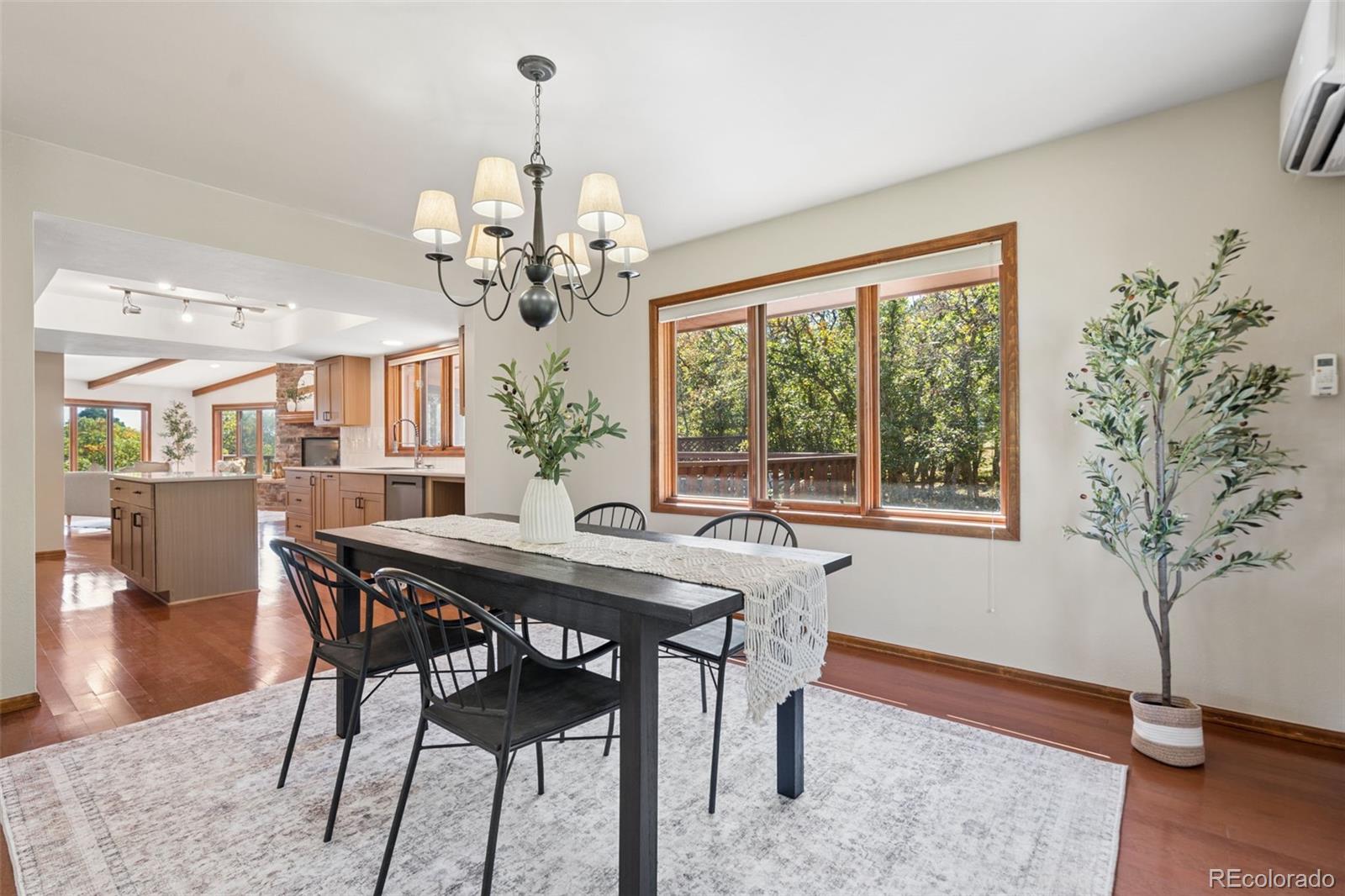 Dining room with a dark table beside large windows, opening to a wood-cabinet kitchen.