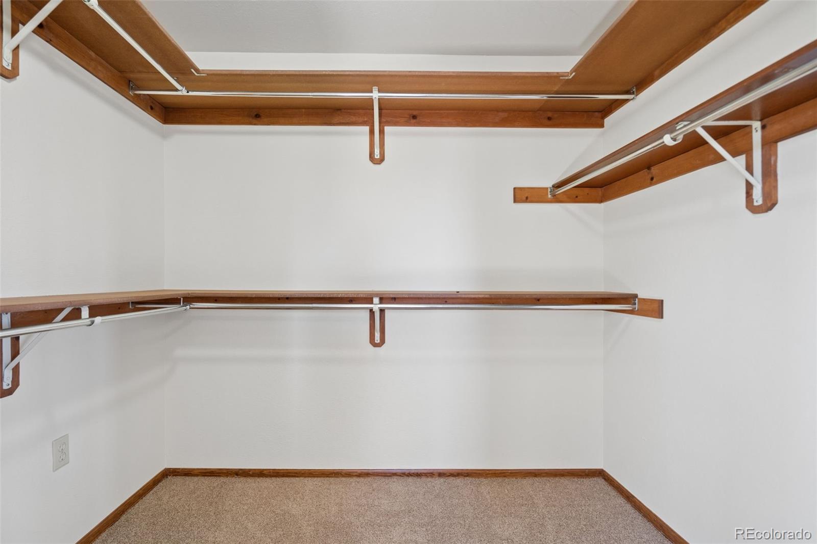 Empty walk-in closet with wood shelves and hanging rods along three walls.