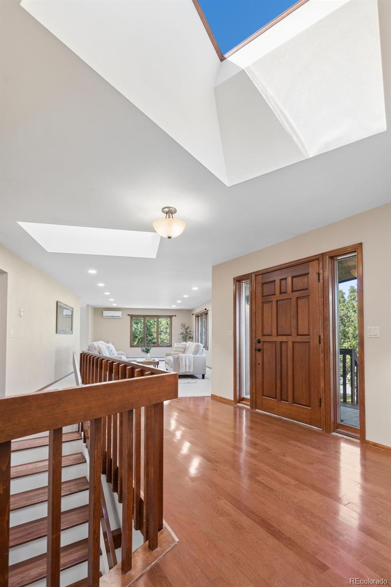 Home foyer with a wooden staircase railing, hardwood floors, and a large skylight.