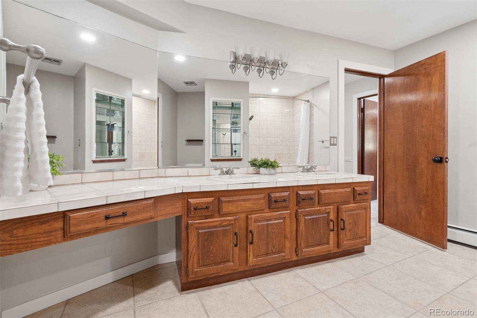 Bathroom with double sinks, mirrored walls, and warm wood vanity cabinets.