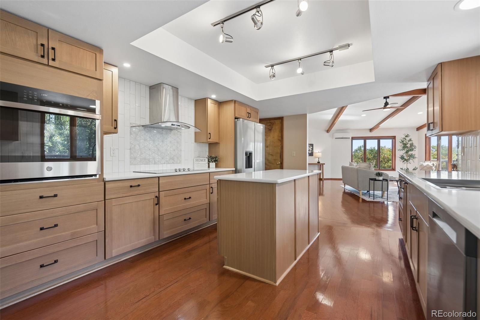 Remodeled kitchen with light wood cabinets, a white island, patterned tile backsplash, and hardwood floors.