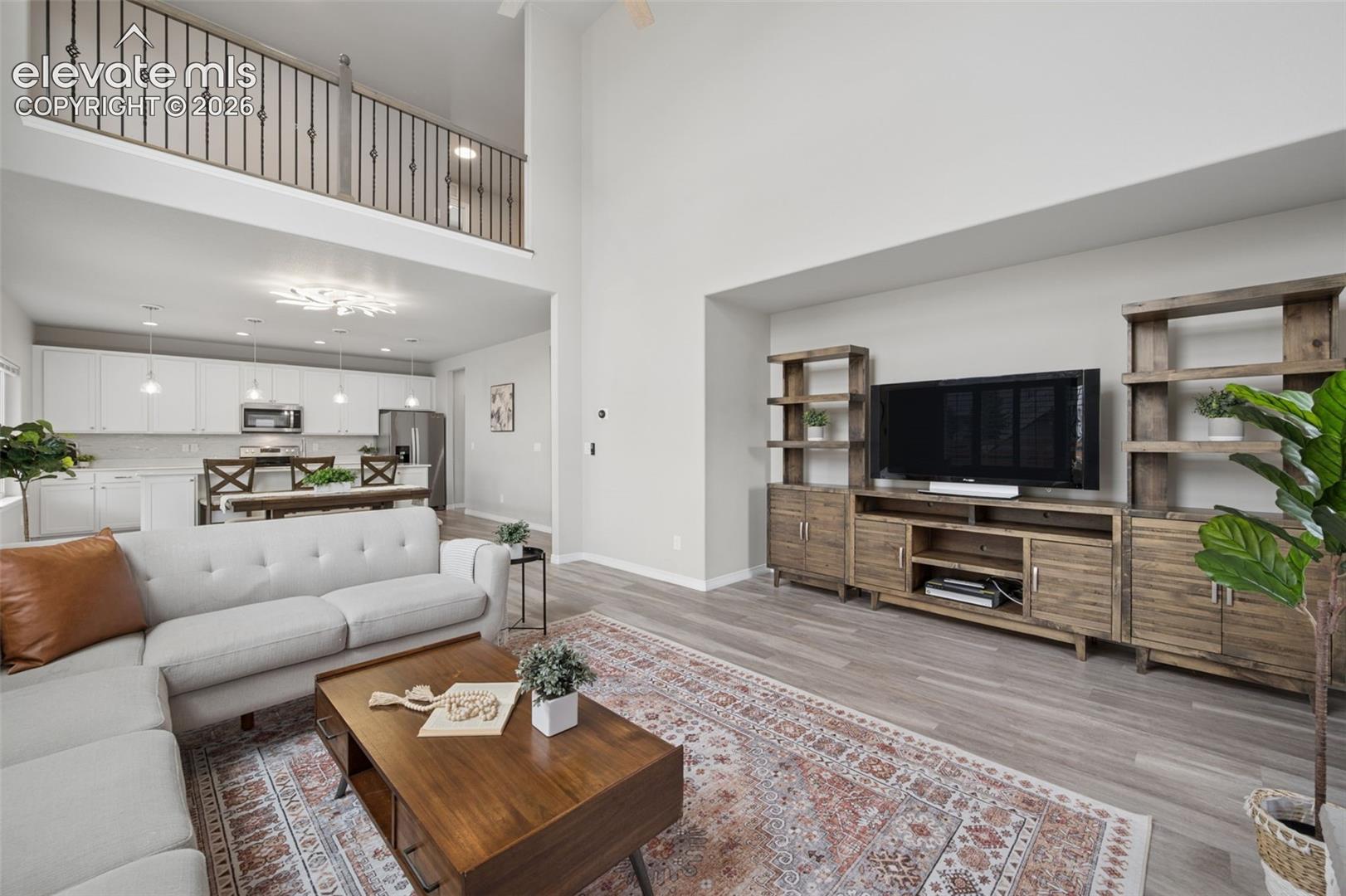 Staged living room with a two-story ceiling, open kitchen, and rustic wood entertainment center.