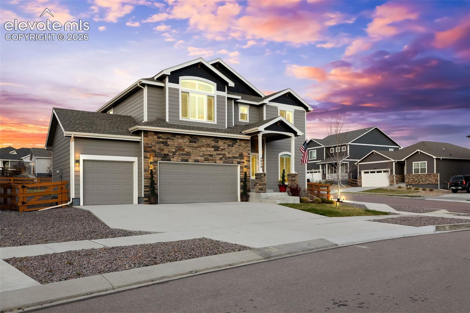 Two-story gray home with stone accents, a double garage, and glowing windows at dusk.