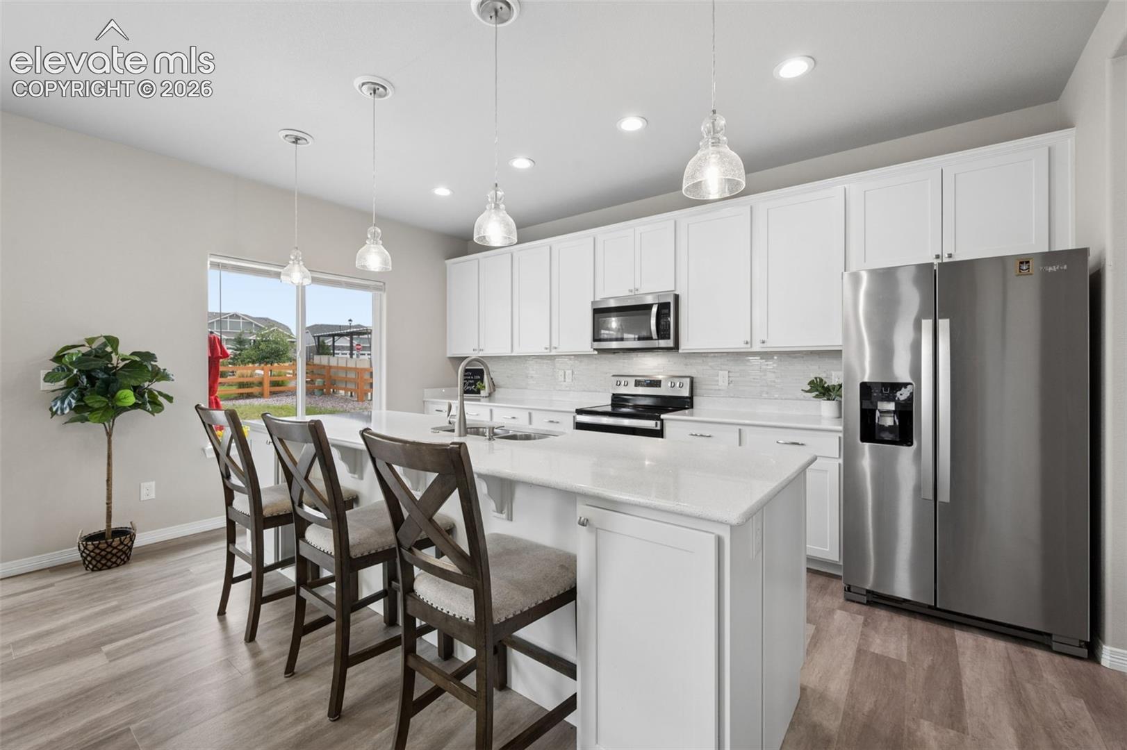 Kitchen with a large white island, dark stools, stainless appliances, and a sliding glass door to the yard.