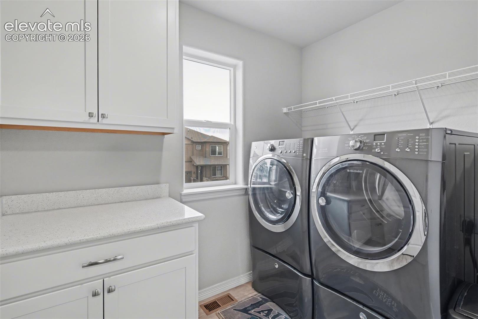 Laundry room with gray front-loading appliances, white cabinetry, and a window.