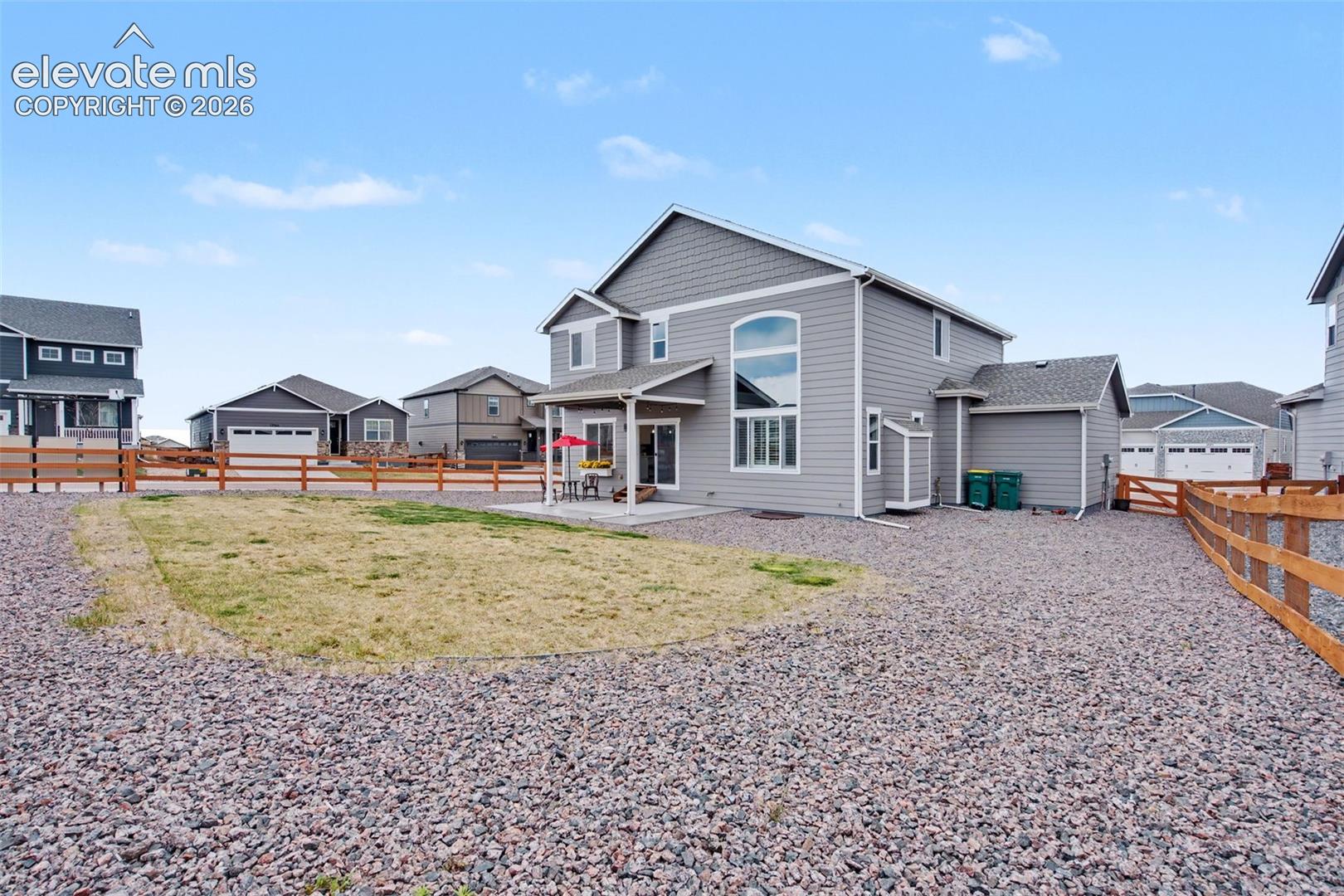 Gray two-story home with a covered patio, fenced backyard, small lawn, and gravel landscaping.