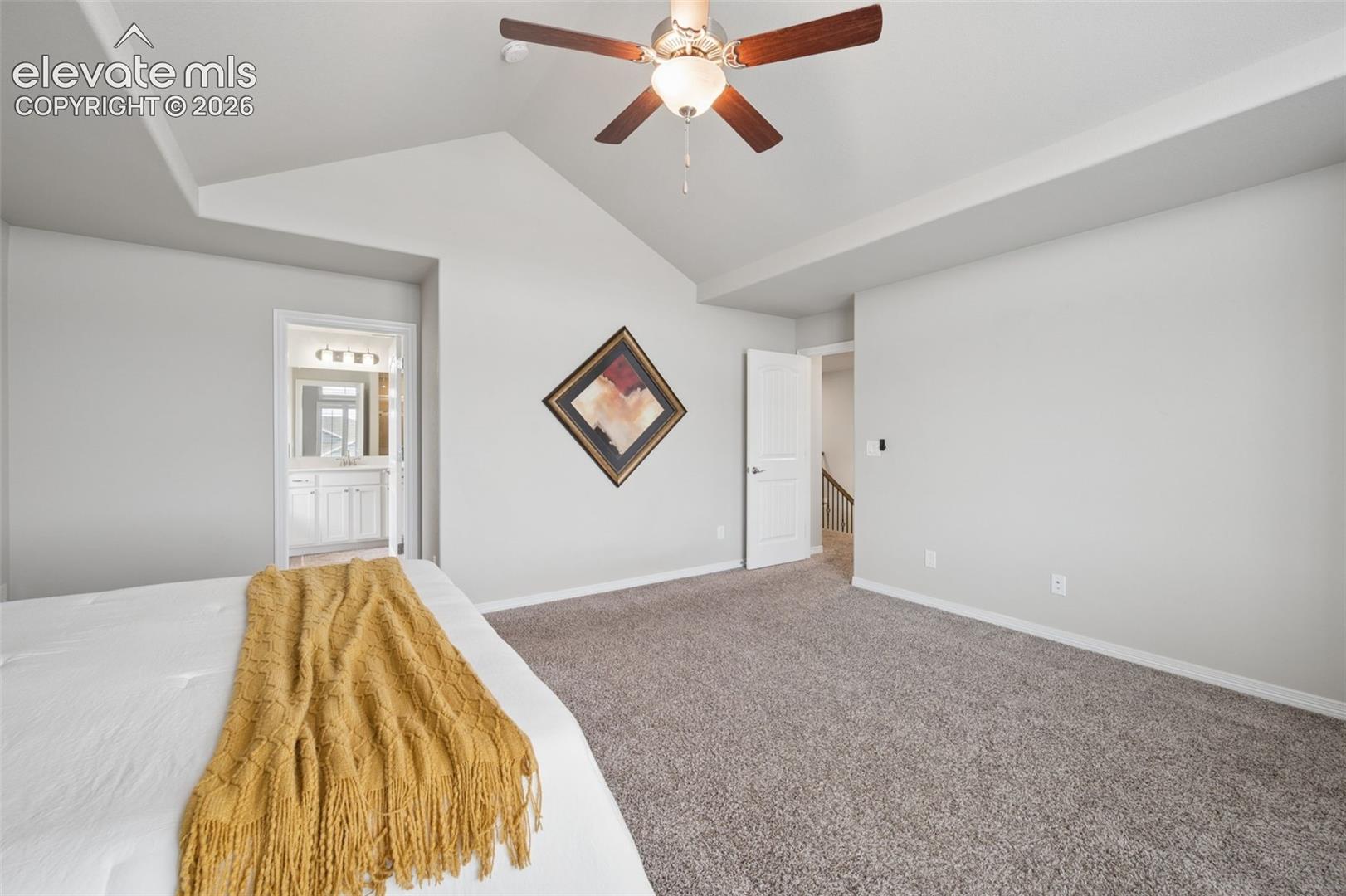 Bedroom with a vaulted ceiling, ceiling fan, and doorway to a bathroom.