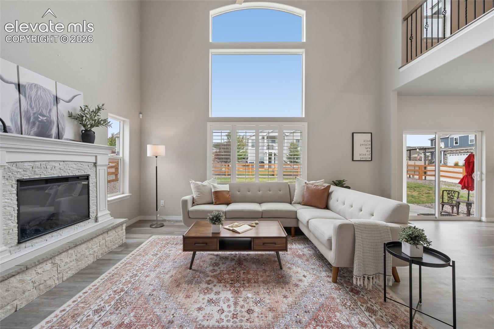 Living room with a vaulted ceiling, stone fireplace, tall windows, and a white sectional sofa.