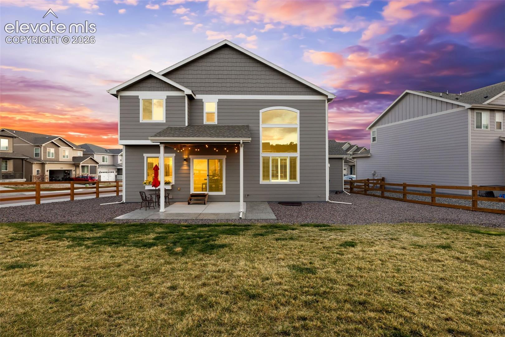 Rear of a gray two-story home with a covered patio and string lights at sunset.