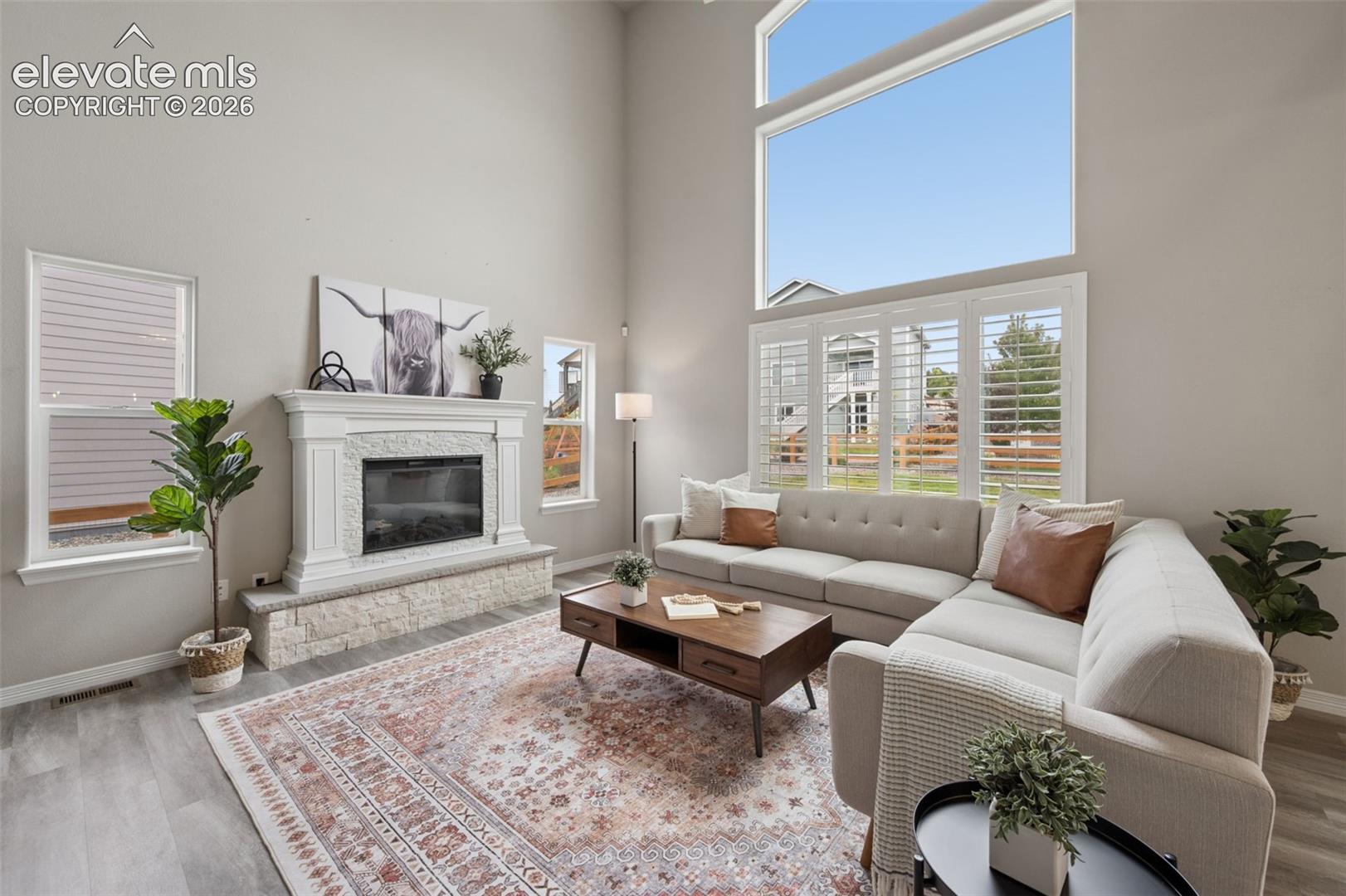 Staged living room with a stone fireplace, tall windows, and a light sectional sofa.