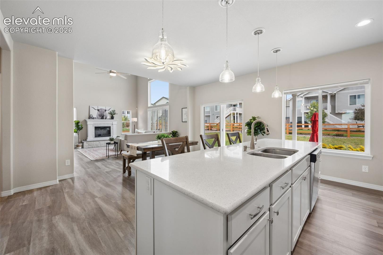 Open-plan kitchen with a large white island, pendant lights, and a living room with fireplace beyond.