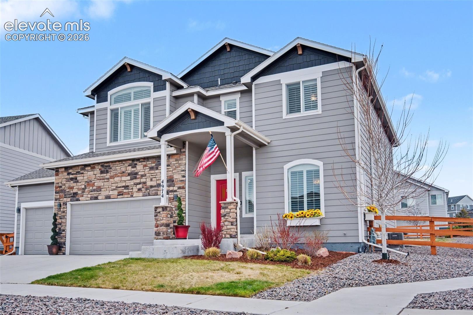 Two-story gray home with a stone facade, red front door, and attached two-car garage.