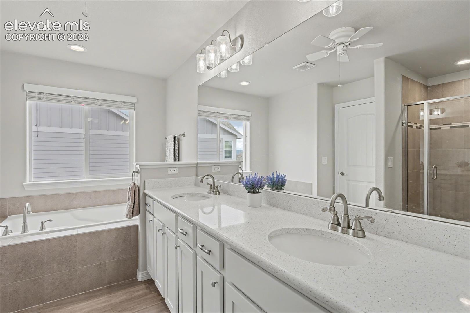 Bathroom with a double-sink vanity, bathtub beneath a window, and glass-enclosed tiled shower.