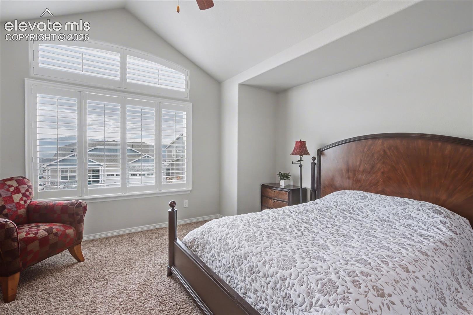 Bedroom with a dark wood bed, white patterned quilt, and plantation shutters overlooking a distant ridge.