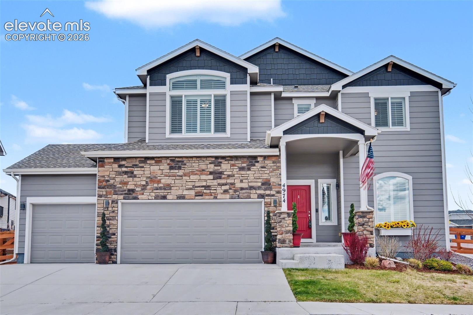 Two-story gray home with a stone facade, red front door, and three-car garage.