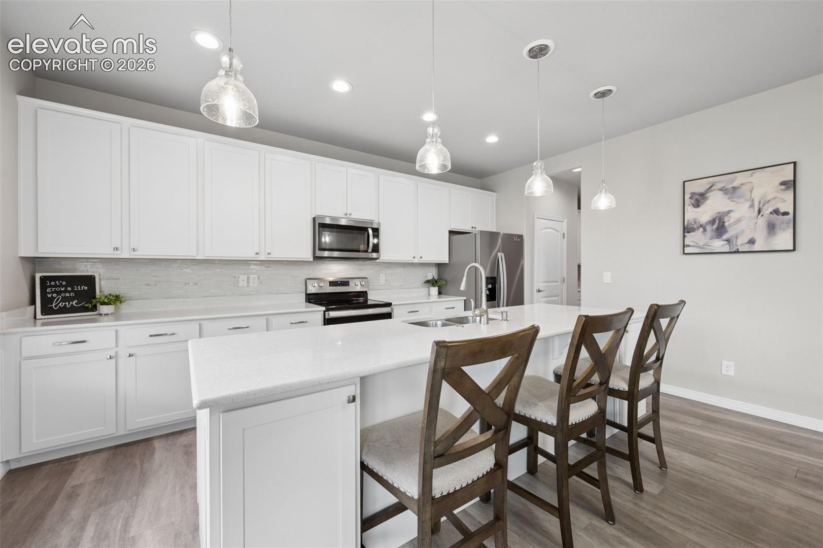 Kitchen with white cabinets, stainless appliances, and a large island with three wooden bar stools.