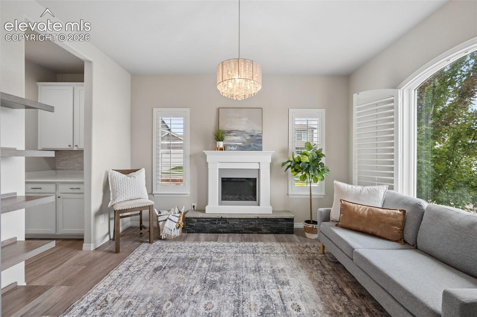 Staged living room with a white fireplace, gray sectional, built-in shelves, and a large arched window.