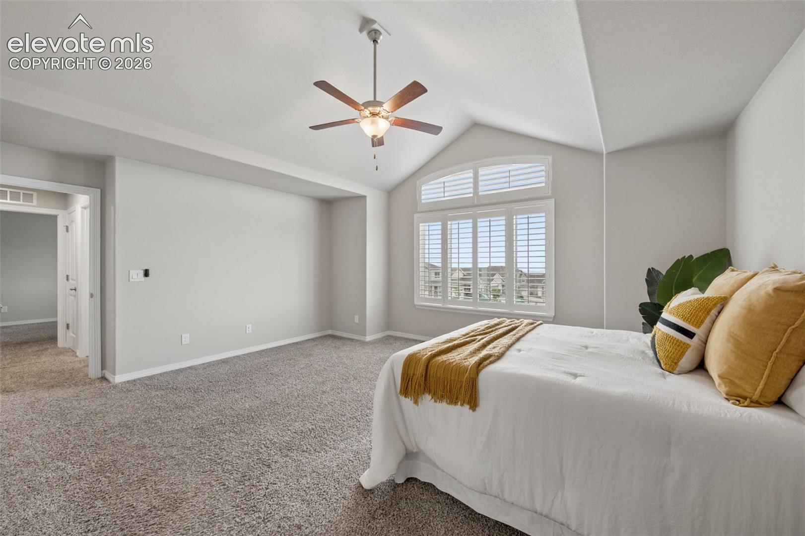 Furnished bedroom with vaulted ceiling, ceiling fan, shuttered windows, and a bed with mustard accents.