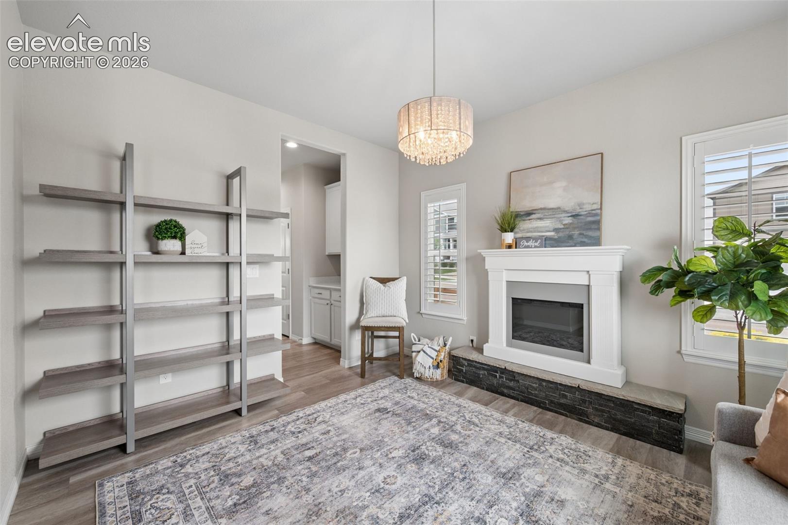 Living room with a white fireplace, dark stone hearth, open shelving, and crystal chandelier.