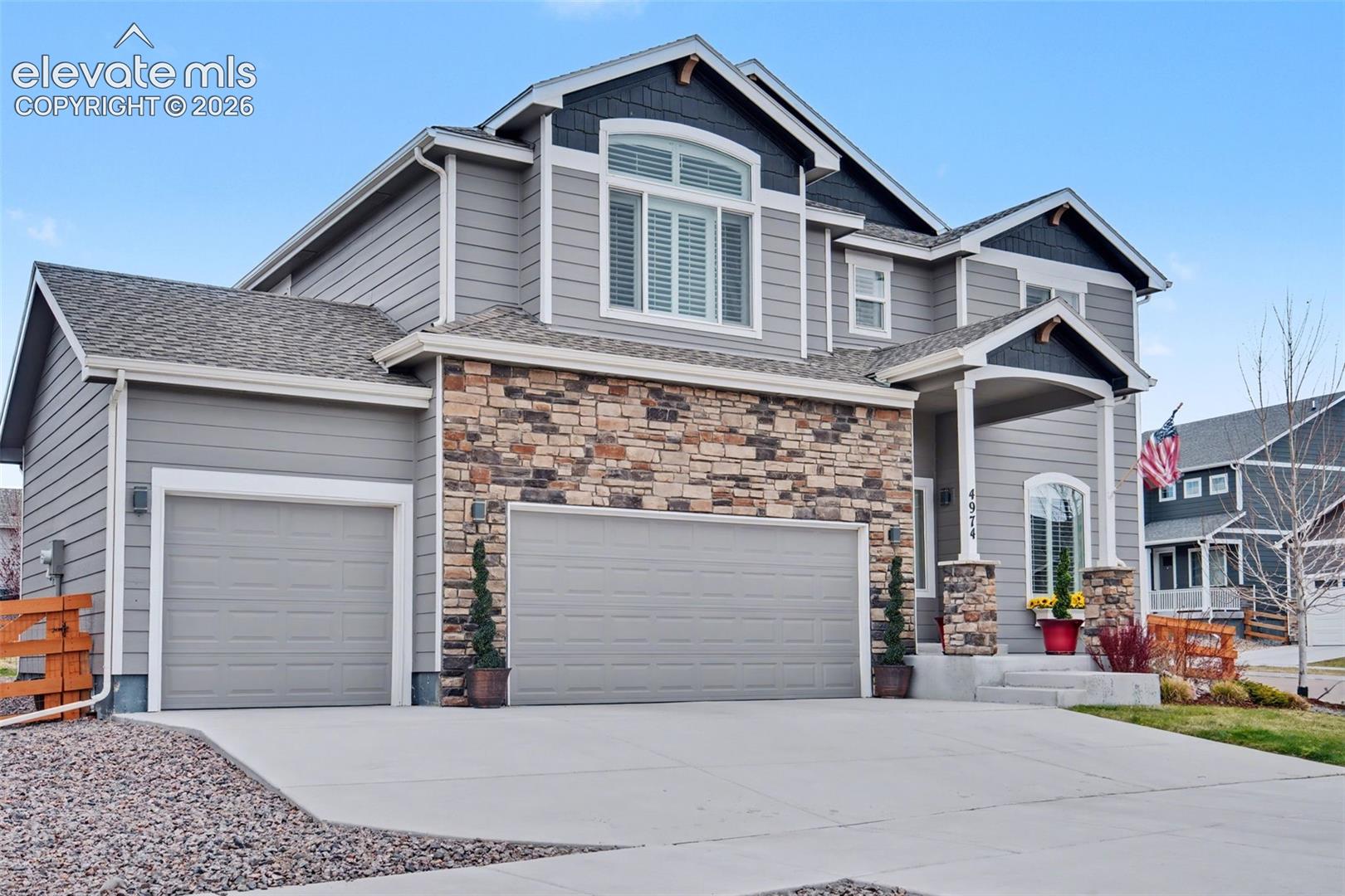 Two-story gray house with stone accents, two garages, and a covered entry displaying a U.S. flag.